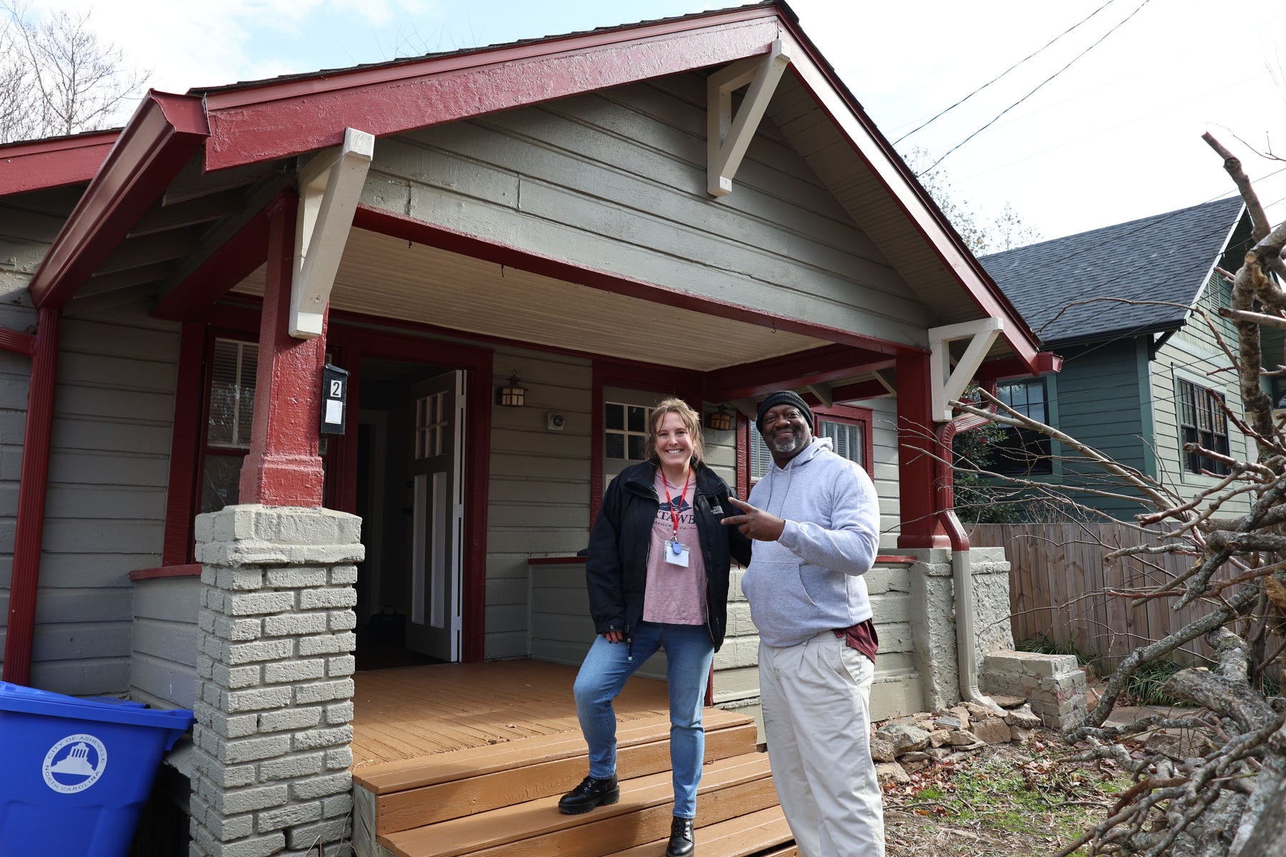 Two people smiling and standing outside a craftsman home.