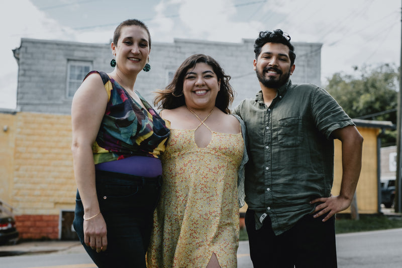 Outside, three people are standing close together smiling at the camera