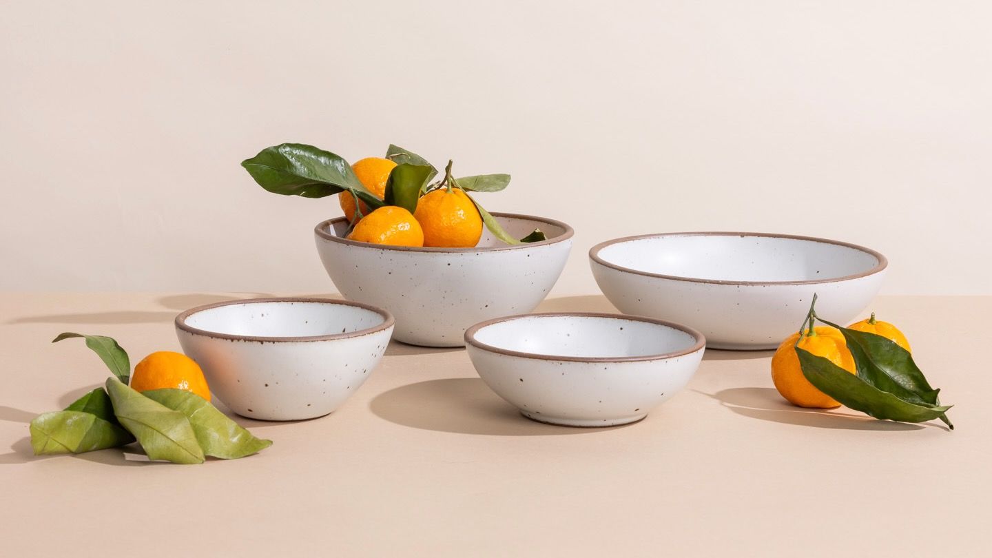 Four different ceramic bowls in a cool white color with oranges with green leaves, against a light background