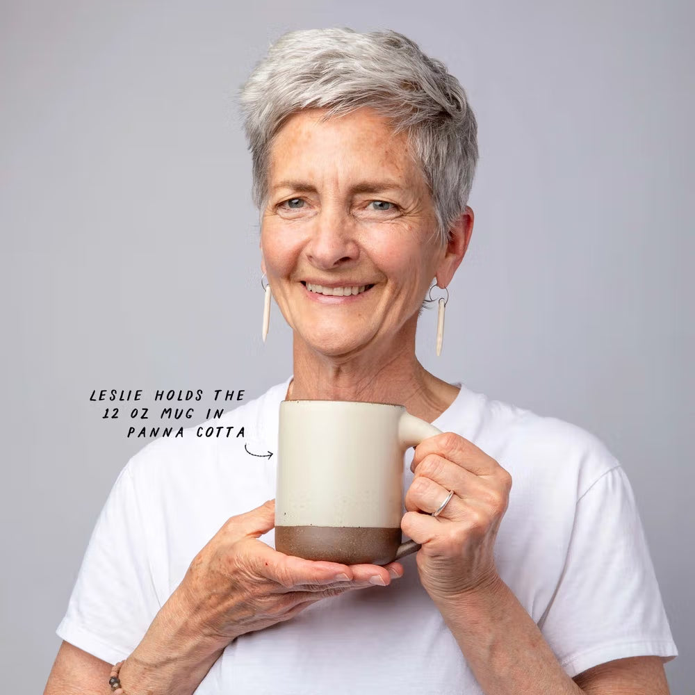 Woman with short gray hair holds The Mug and smiles