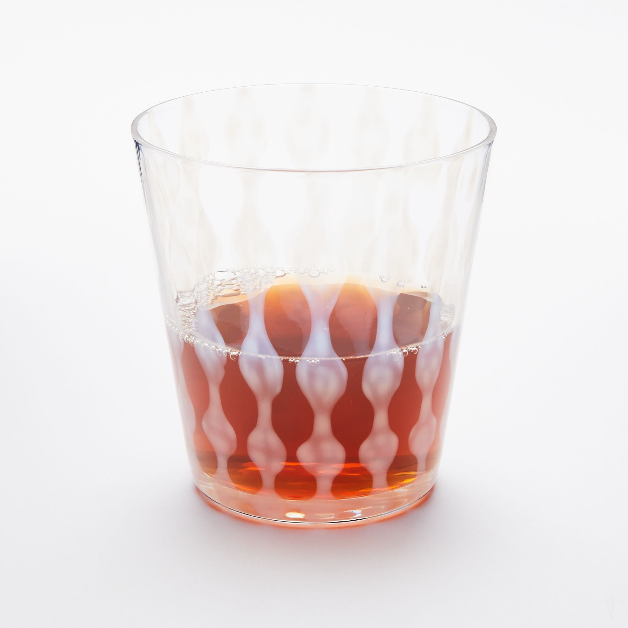 A short clear glass with a delicate vertical wave pattern, half filled with a drink