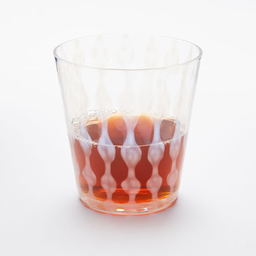 A short clear glass with a delicate vertical wave pattern, half filled with a drink