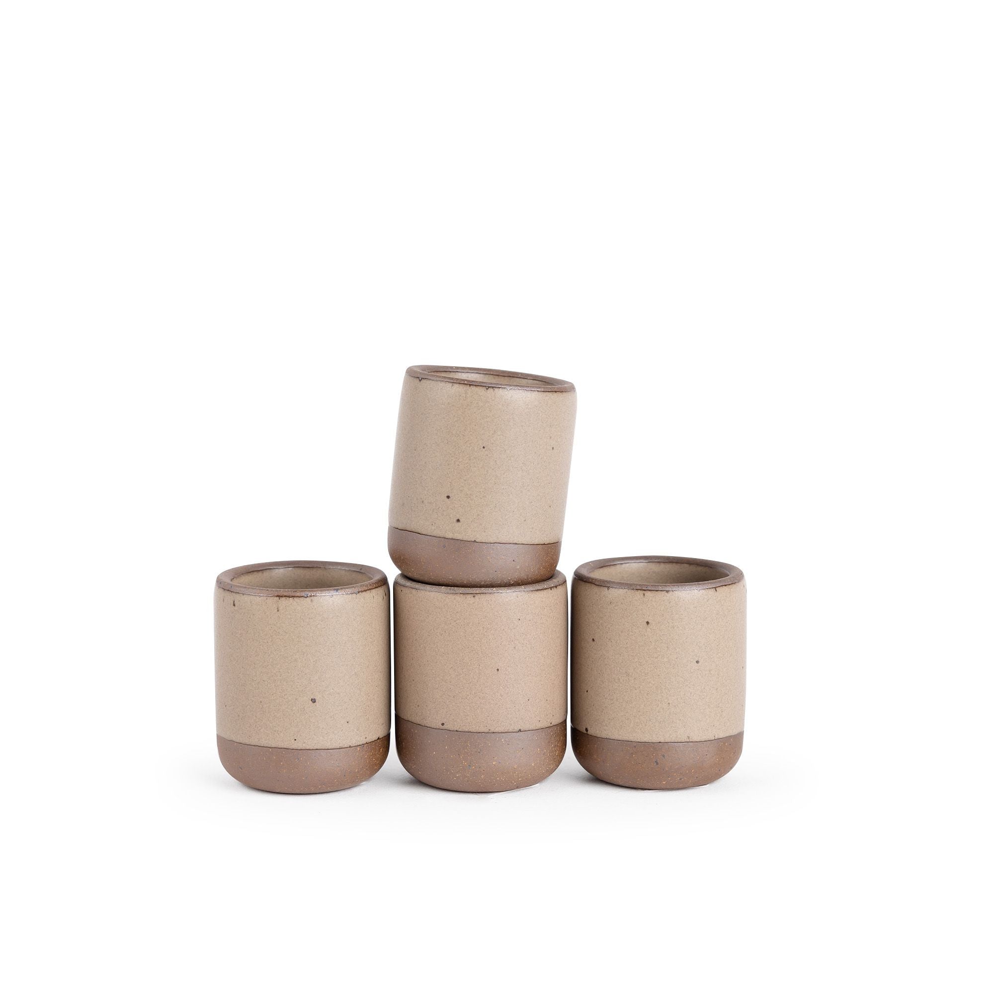 A set of 4 small, short ceramic mug cups in a warm pale brown color featuring iron speckles and unglazed rim and bottom base, stacked in a row of 3, with the 4th on top.