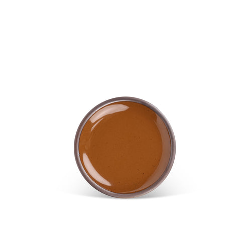 A dessert sized ceramic plate in a glossy caramel brown color featuring iron speckles and an unglazed rim.