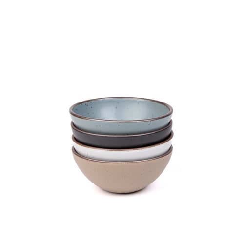 A stack of 4 medium sized rounded ceramic bowls in a blue-grey, graphite black, cool white, and warm pale brown colors featuring iron speckles and an unglazed rim