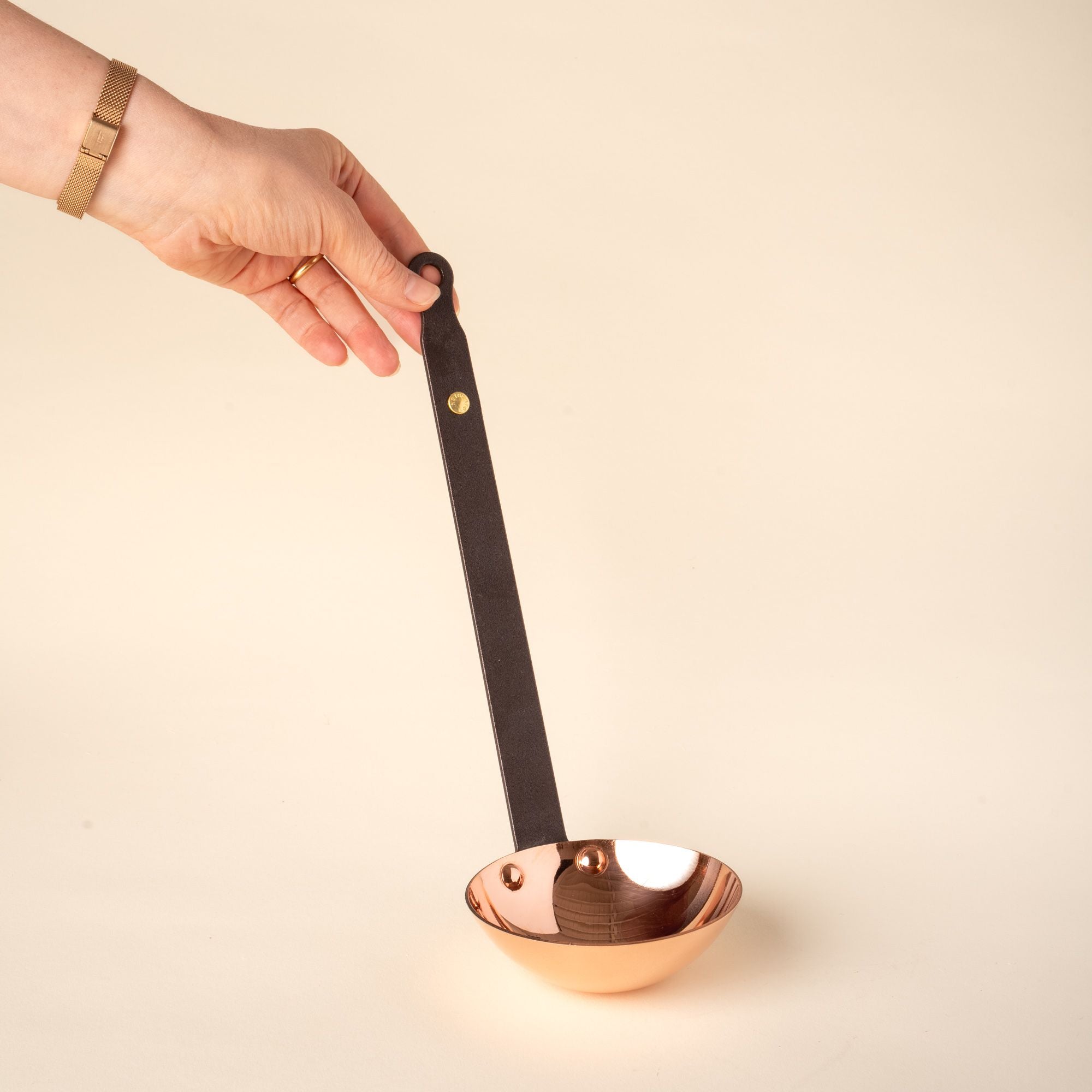A hand holds up a copper ladle with a long black handle