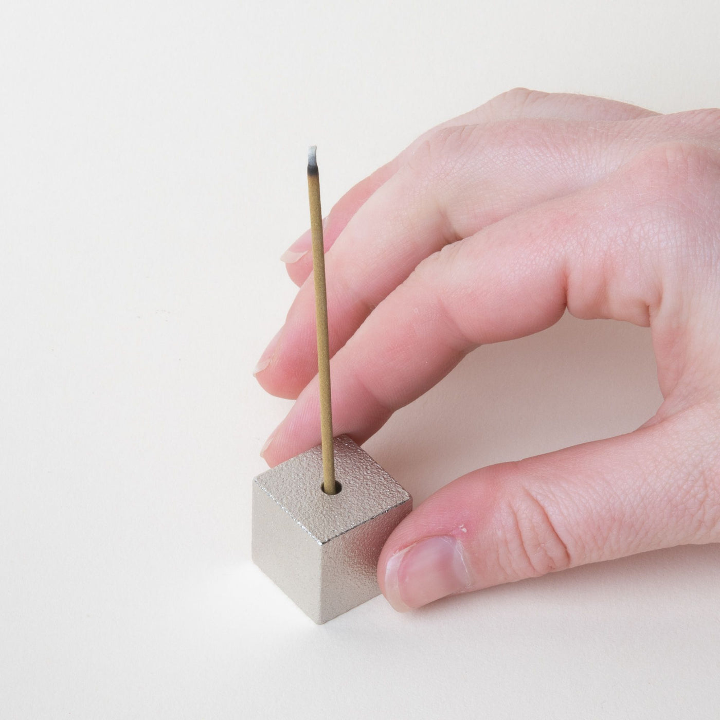 Hand holding a minimal cube made of pewter with incense sitting on top