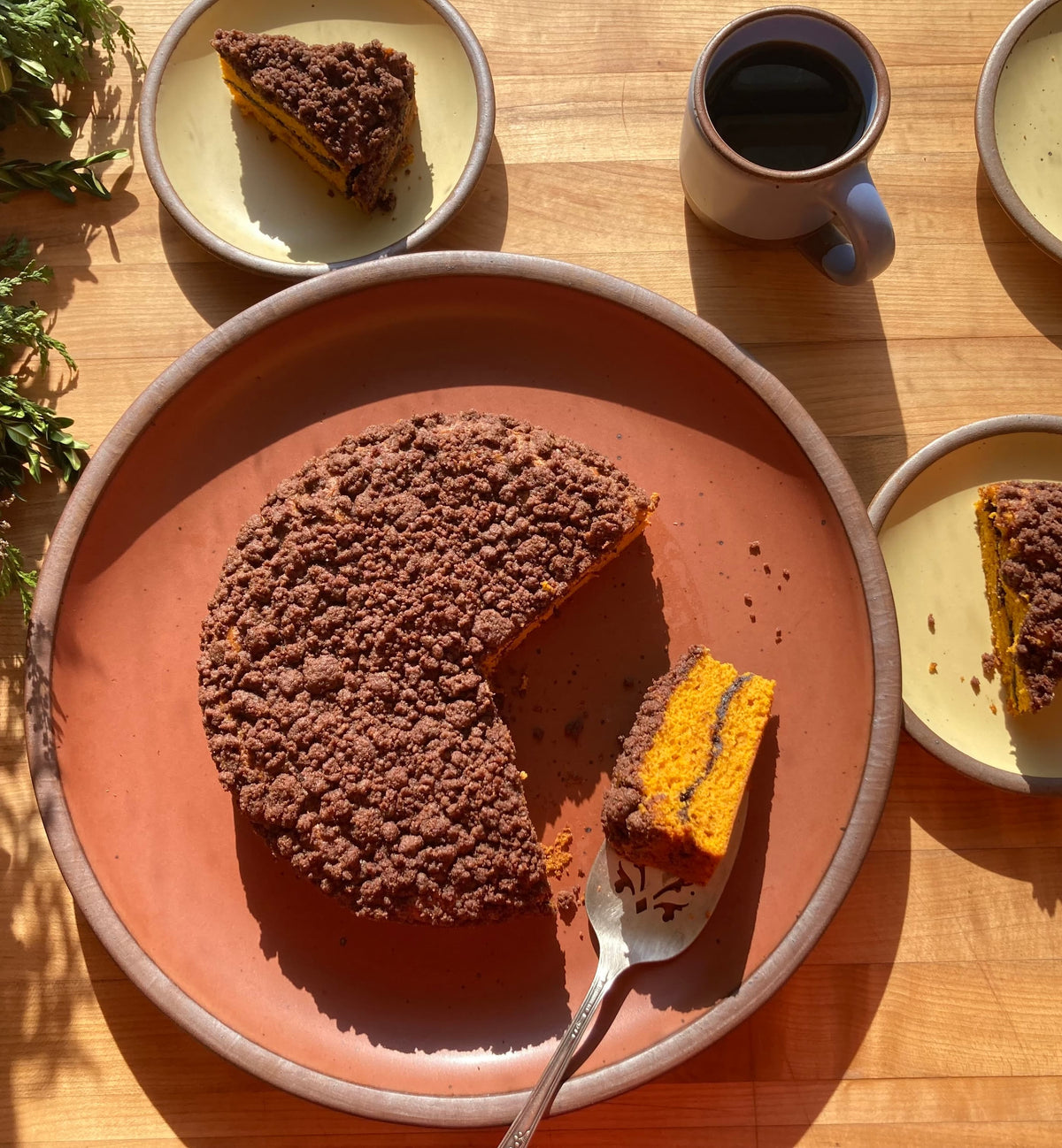 A butternut coffee cake sitting on a terracotta color plate with slices plated on small cake plates in a butter color.