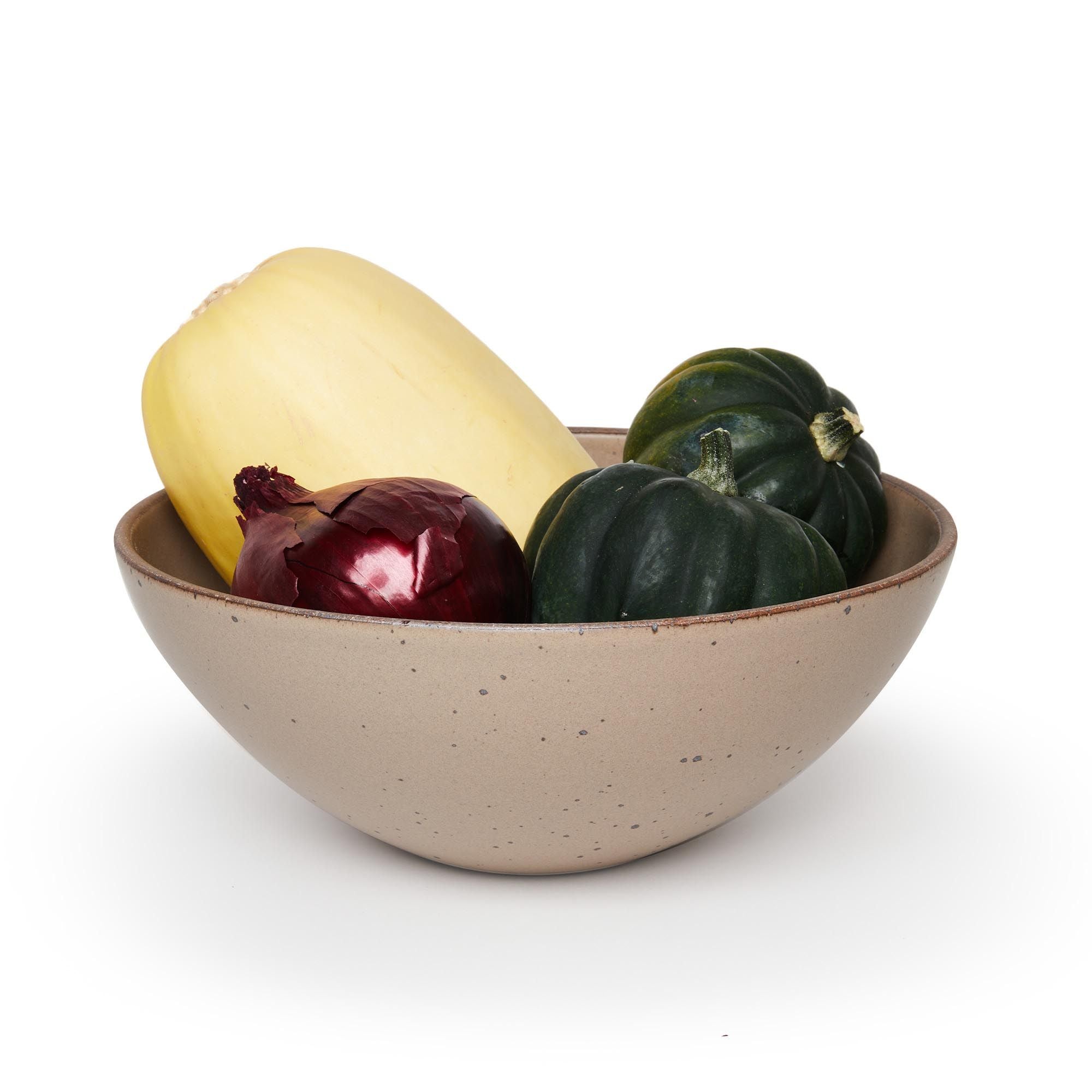A large ceramic mixing bowl in a warm pale brown color featuring iron speckles and an unglazed rim, filled with a medley of vegetables
