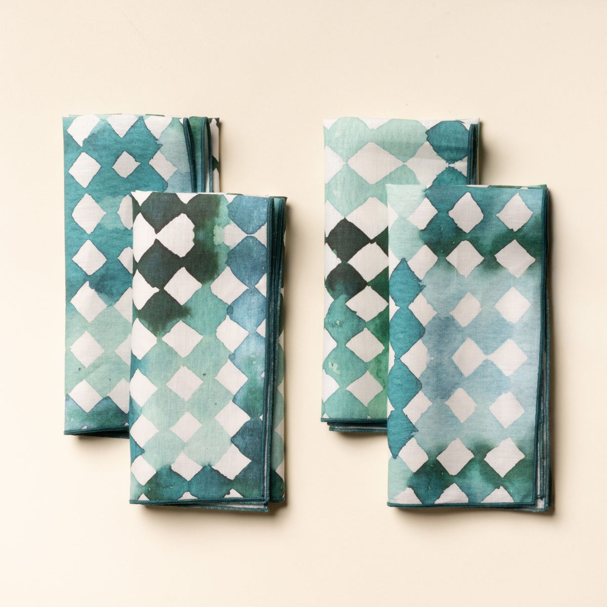 Set of folded watercolor diamond-patterned cloth napkins in green and teal tones