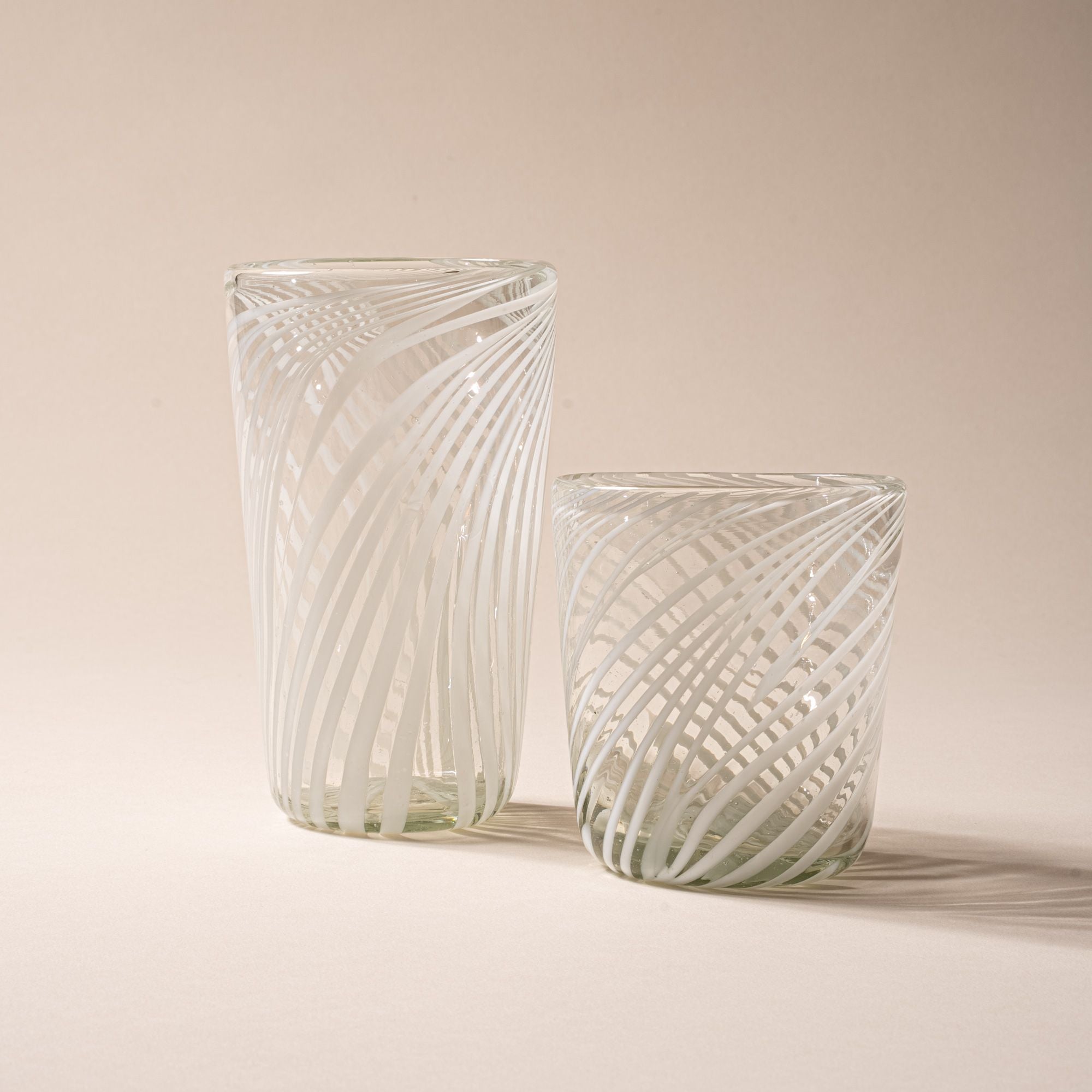 Clear glass tumbler and pint glass with white diagonal swirl pattern on a neutral background.