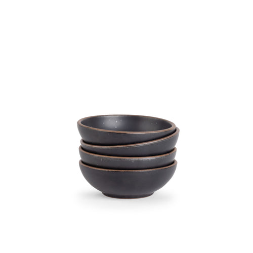A stack of 4 small shallow ceramic bowls in a graphite black color featuring iron speckles and an unglazed rim