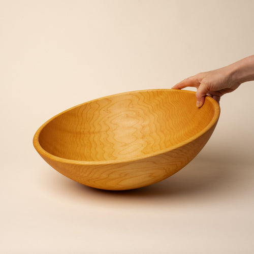 A hand holds out an extra large maple wooden bowl