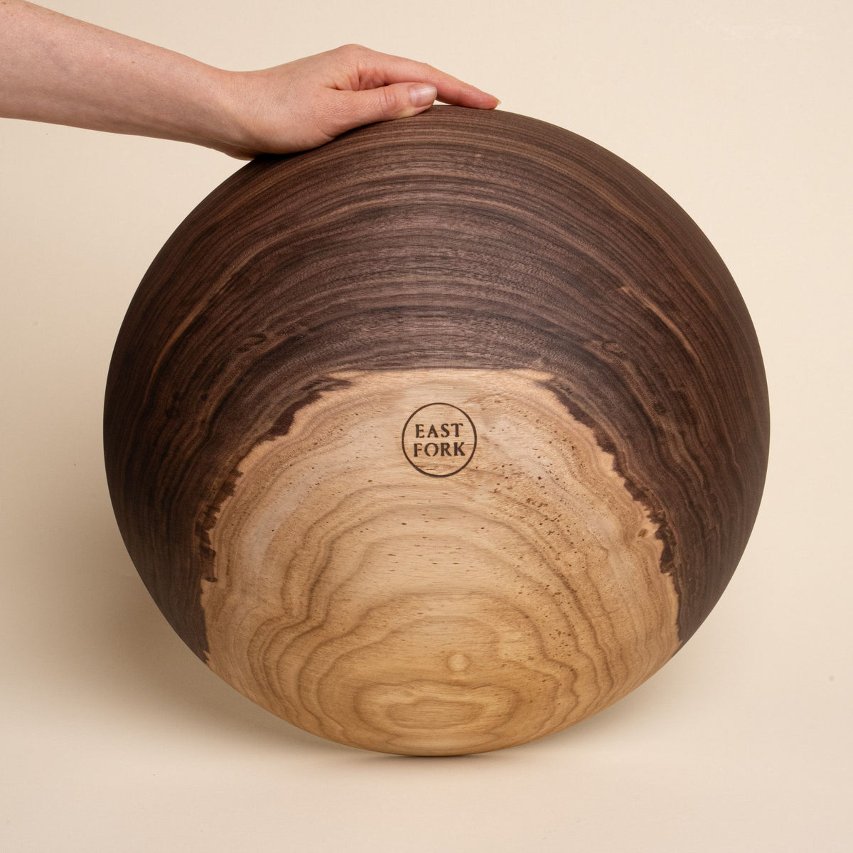 A hand holds up an extra large walnut wooden bowl