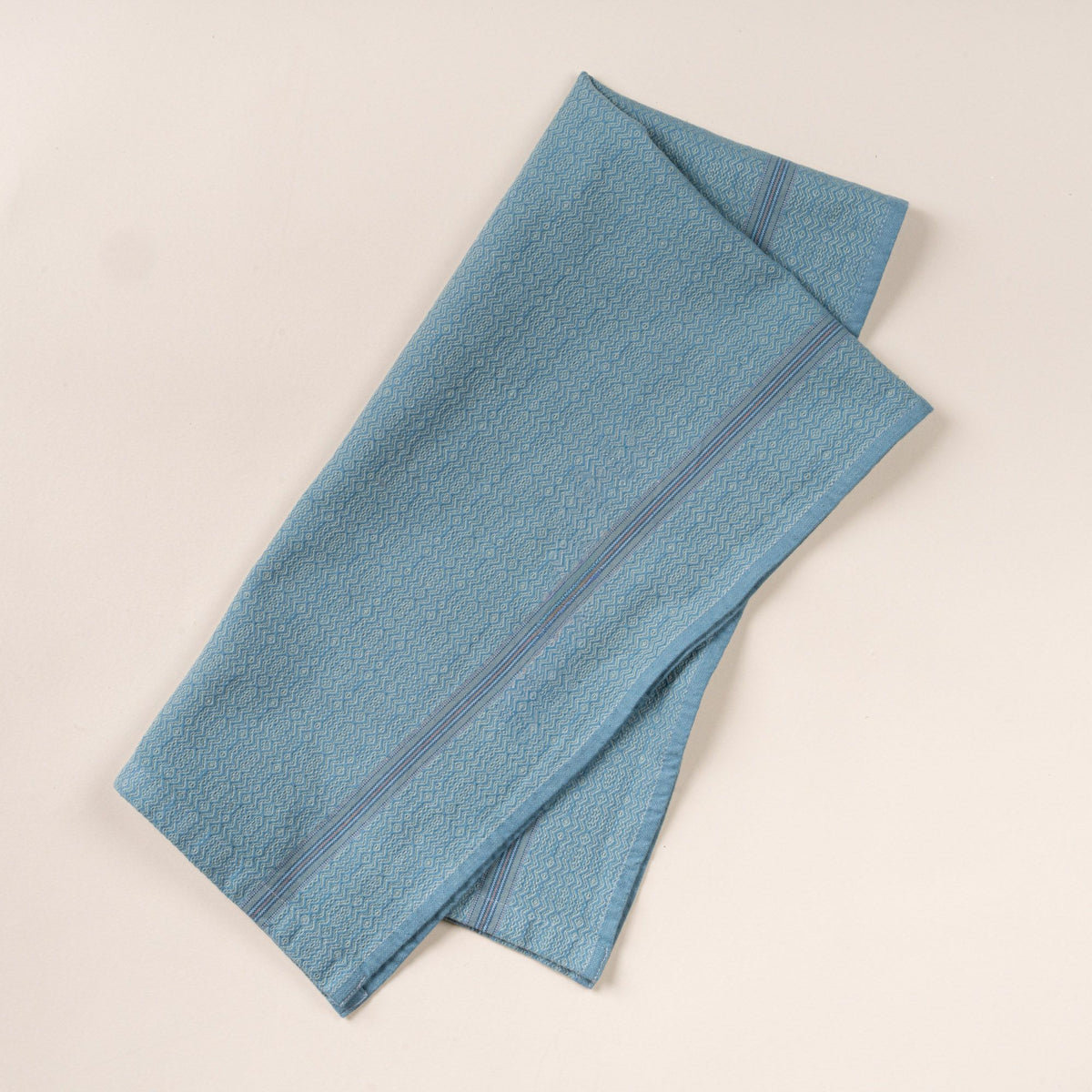 Blue woven kitchen towel with a subtle textured pattern and slim striped accent, folded neatly on a clean neutral background.