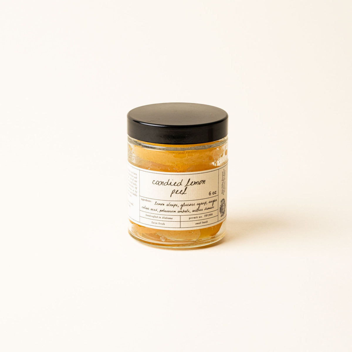 A jar of candied lemon peel with a minimalist label and black lid, set against a soft cream background.