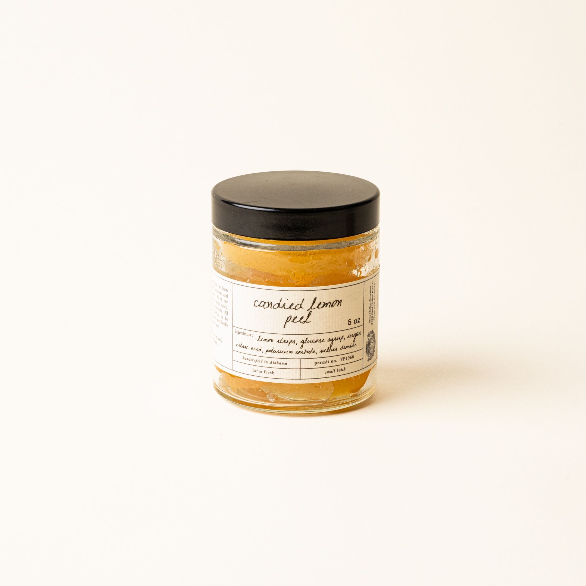 A jar of candied lemon peel with a minimalist label and black lid, set against a soft cream background.