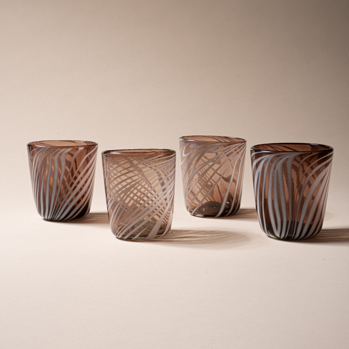 Four smoky brown glass tumblers with white diagonal swirl pattern on a neutral background.