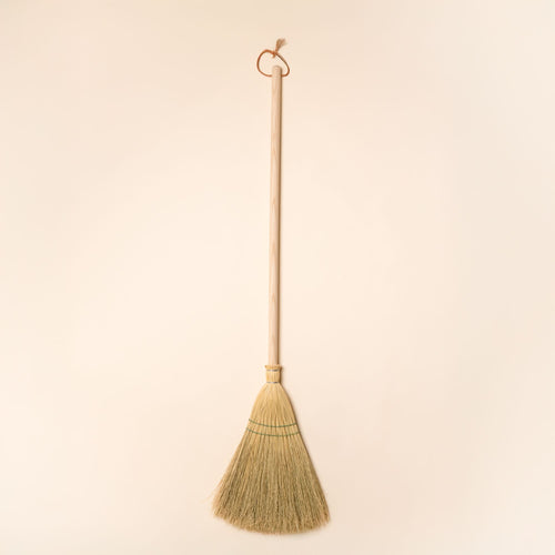 A solid maple wood broom with a leather loop at the top for hanging.