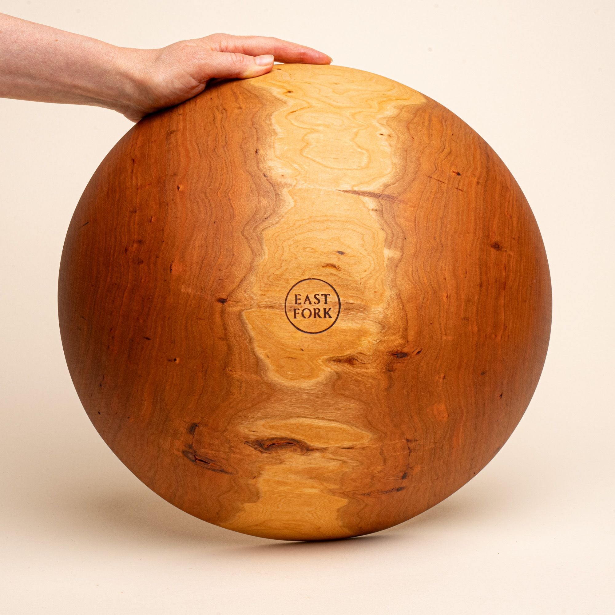A hand holds up an extra large cherry wooden bowl