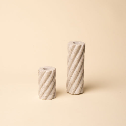 Pair of cream stone candle holders with spiral ridges, one tall and one short, set against a beige backdrop.