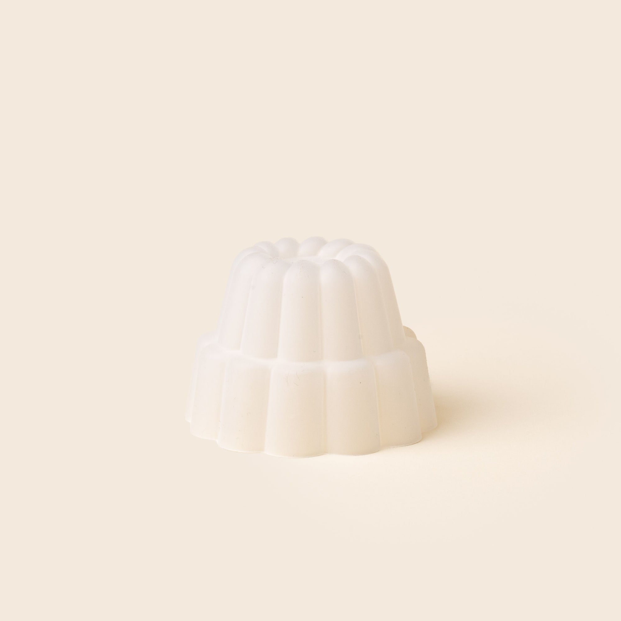 A small, white, fluted jelly-shaped mould for dessert set against a soft beige background.