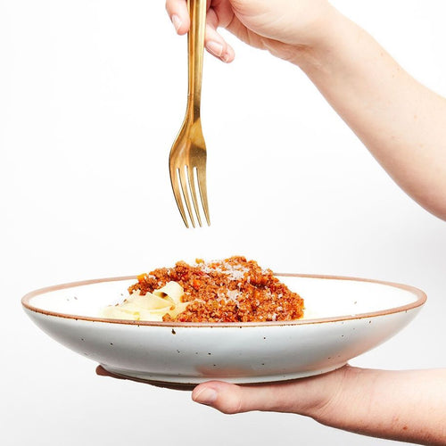 A hand holds a white ceramic shallow plate bowl combo with pasta inside and another hand holds a fork above.