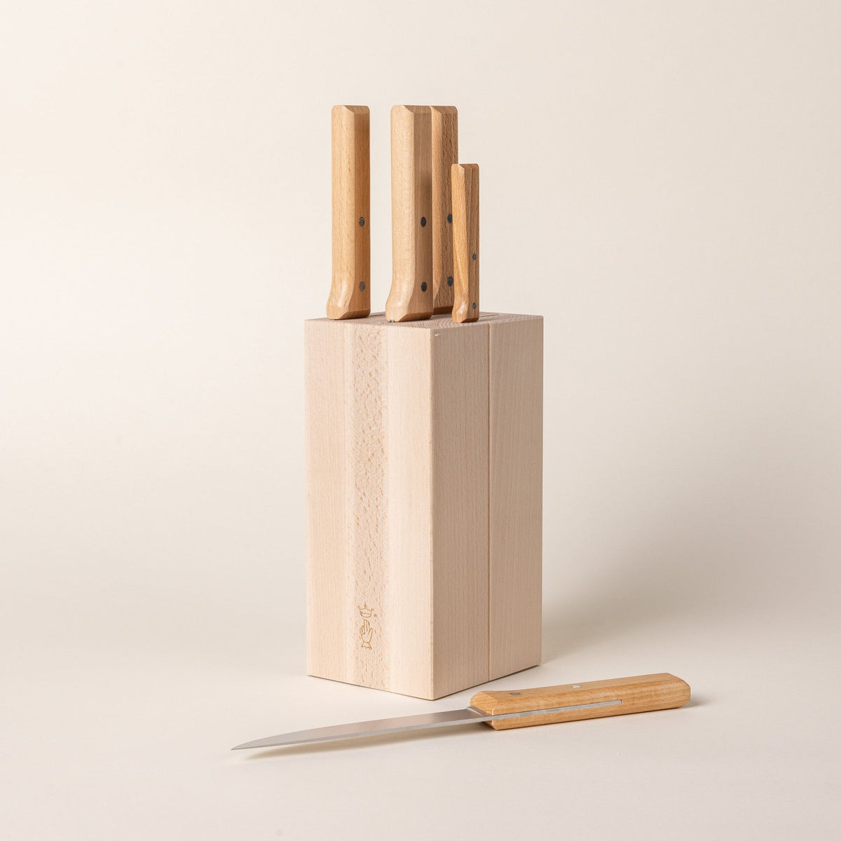 A tall rectangular wooden block with knives inside and the wooden handles sticking out at the top. One knife is laying flat next to the block.