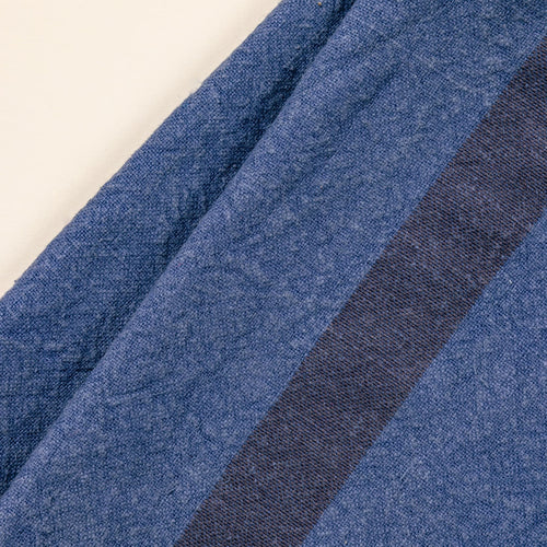 A close up of a folded linen towel in an indigo color with a plum stripe in the middle