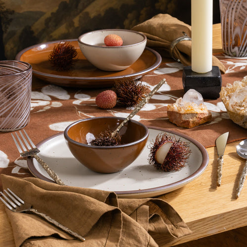 Table set with glossy brown and cream ceramic dishes, rambutan and lychee fruits, crystal clusters, and brass-handled utensils