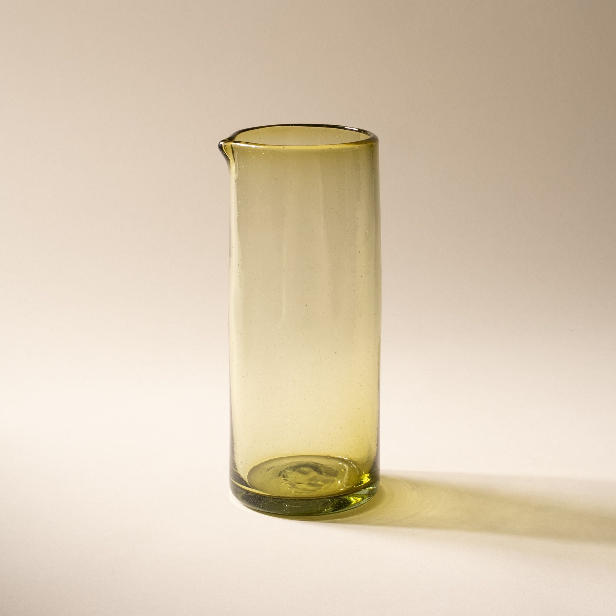 An olive green tall transparent glass pitcher with small spout at the top