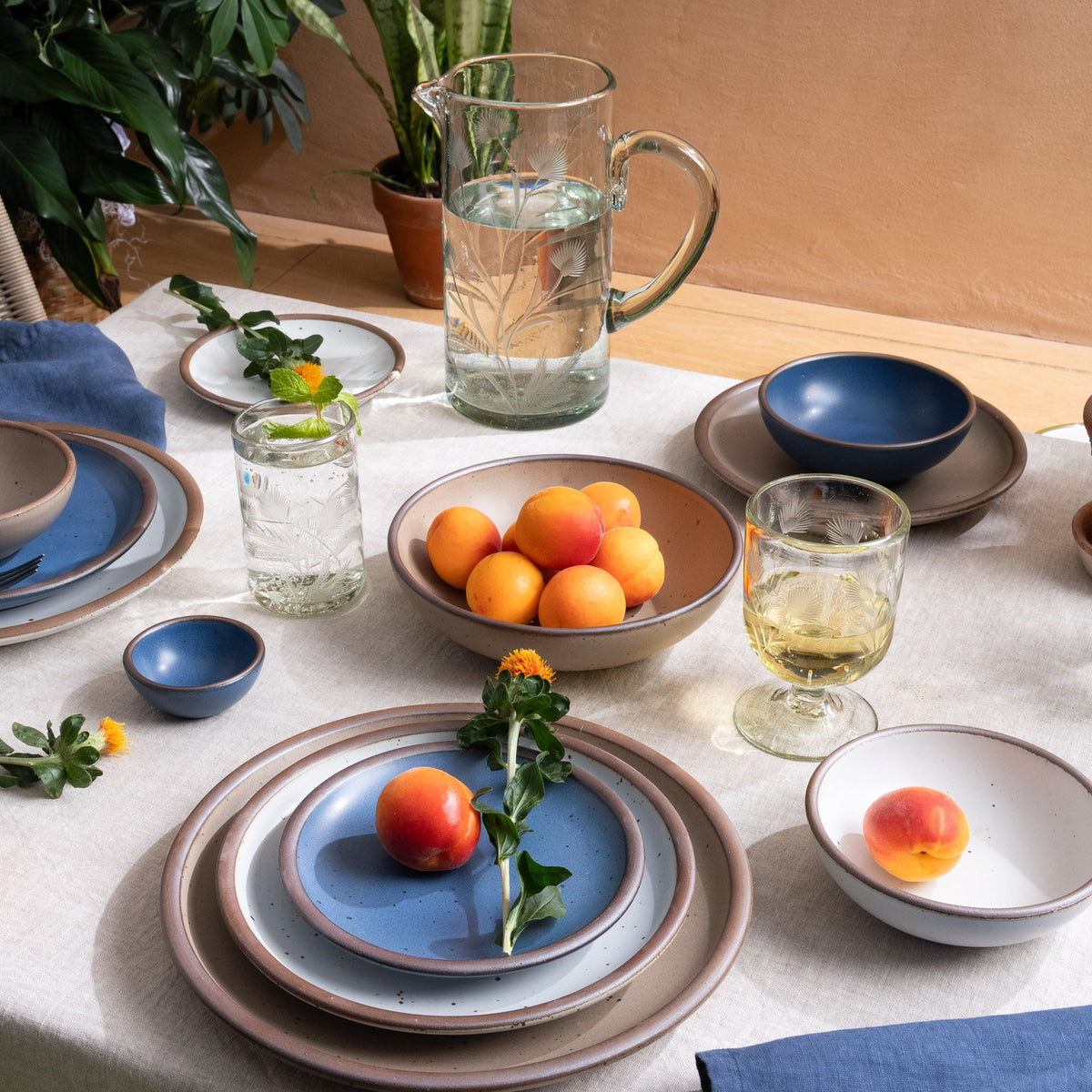 A table with ceramic dinnerware in cool medium blue, white, pale warm brown, and etched thistle glassware