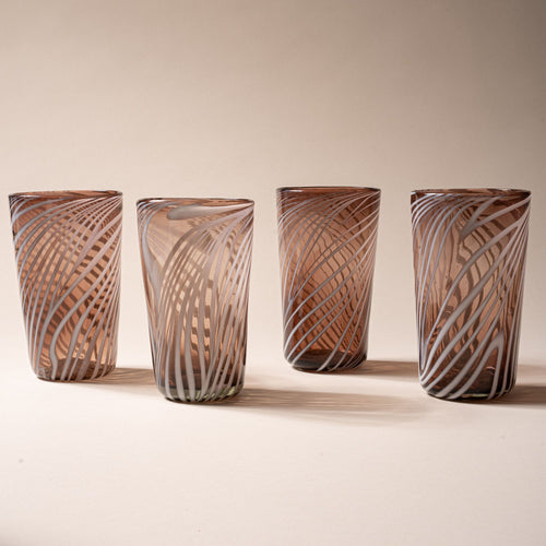 Four smoky brown pint glasses with white diagonal swirl pattern on a neutral background.