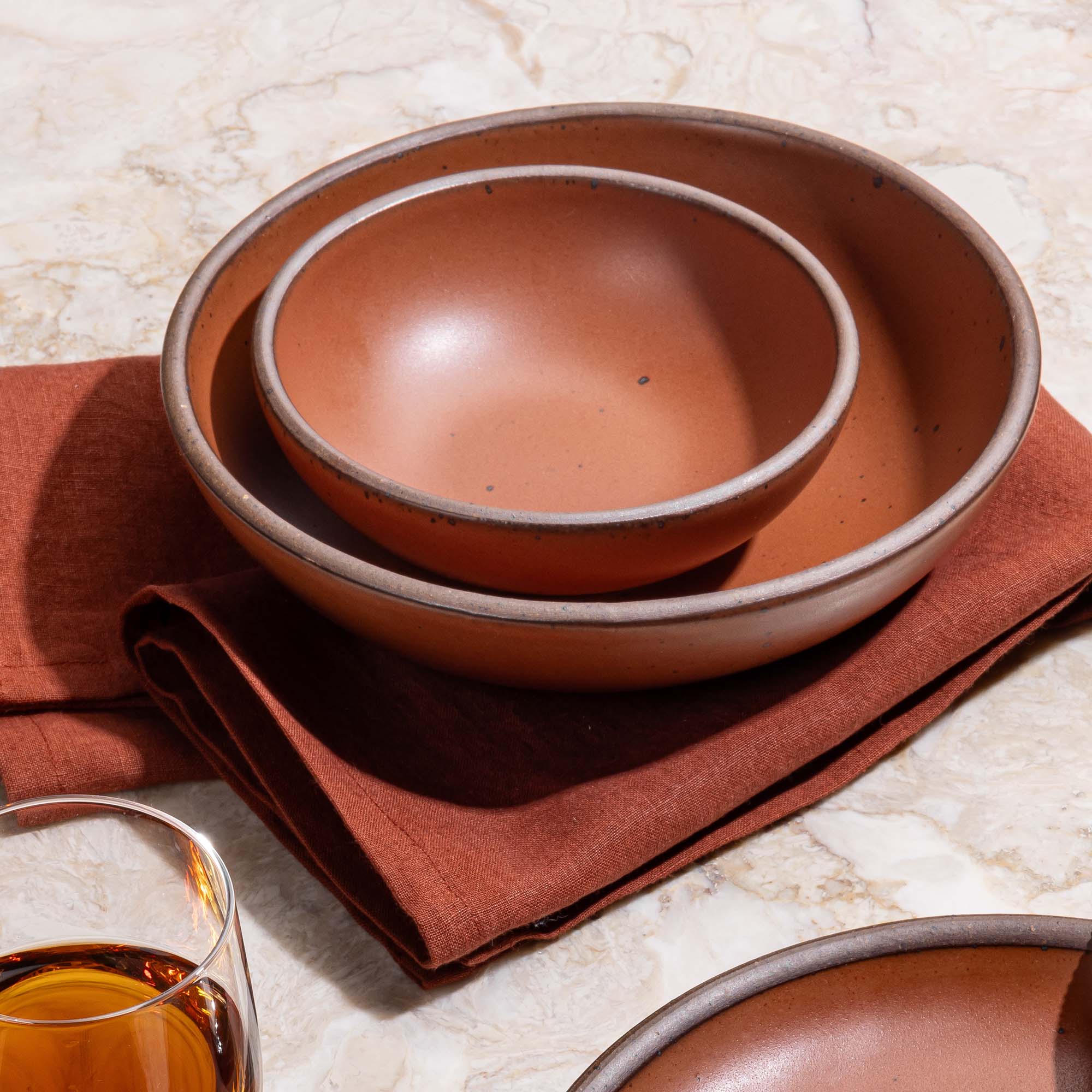 Two nesting ceramic shallow bowls in a cool terracotta color with a napkin in the same color.