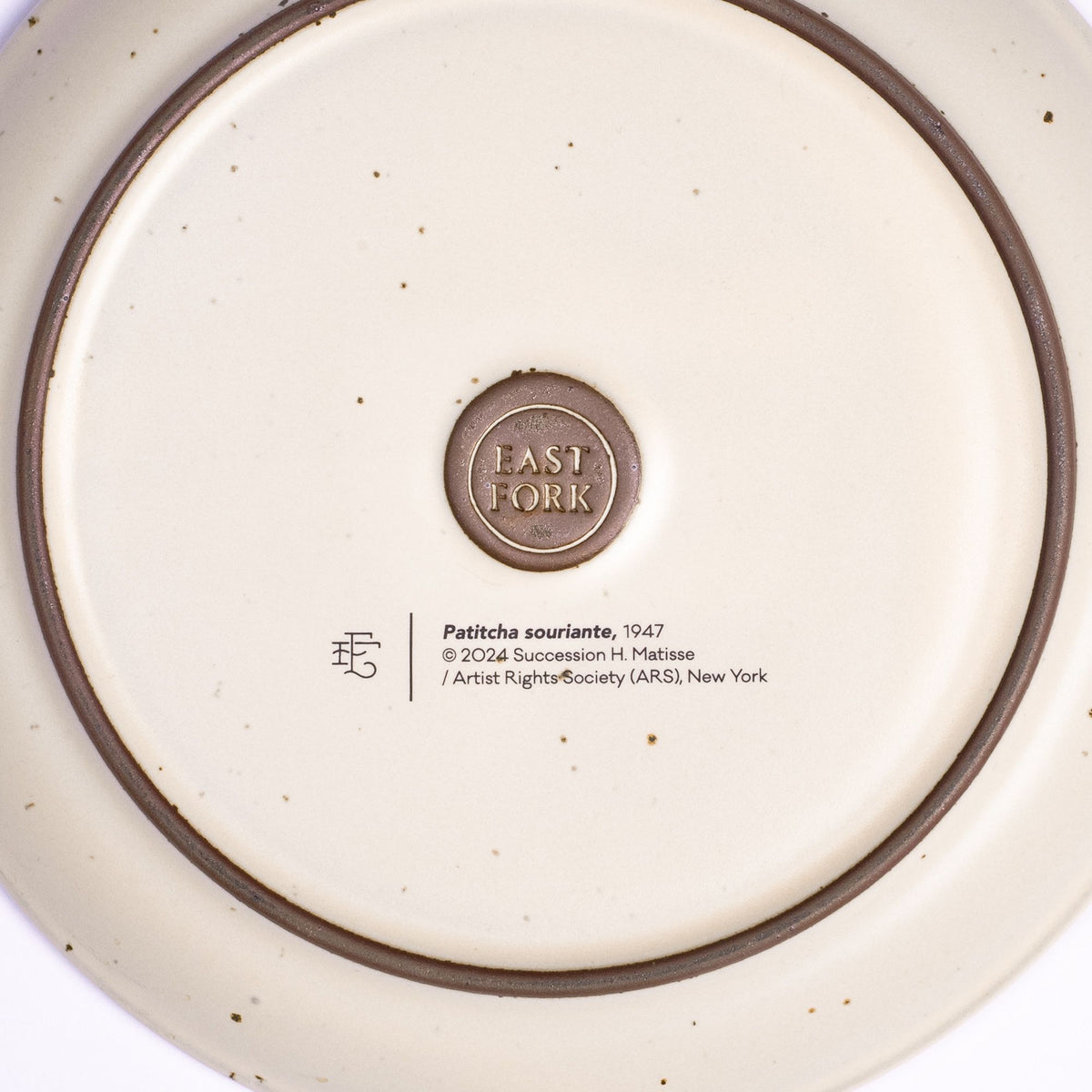 The back of a side plate with an East Fork stamp with a small decal of information about the artwork, Patitcha souriante, by Henri Matisse.