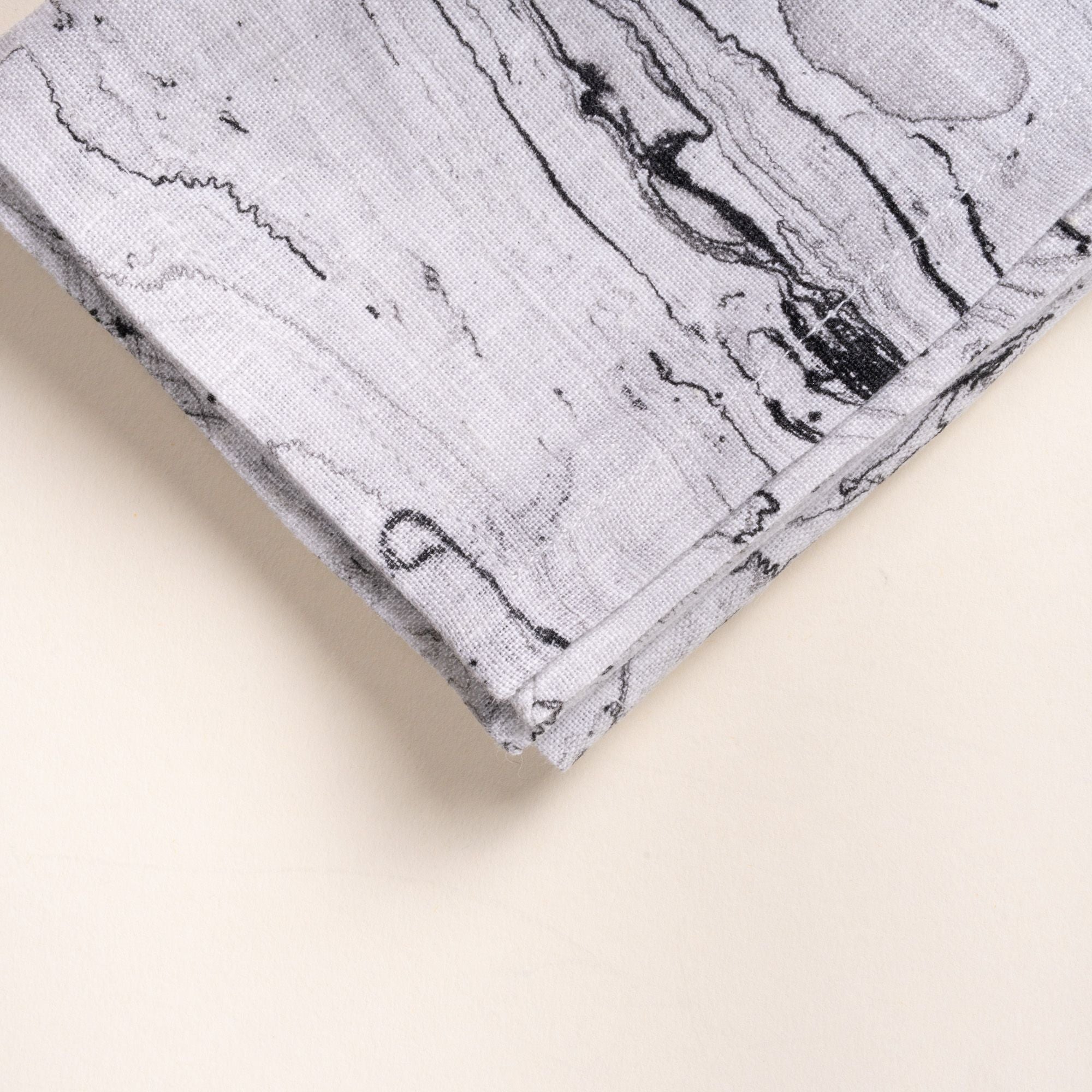 A closeup of the corner of a folded gray marbled cloth napkin with swirling stone-like pattern on a light background.