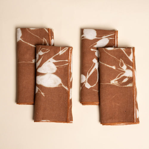 Set of four brown napkins with white botanical print, neatly folded on a neutral background.