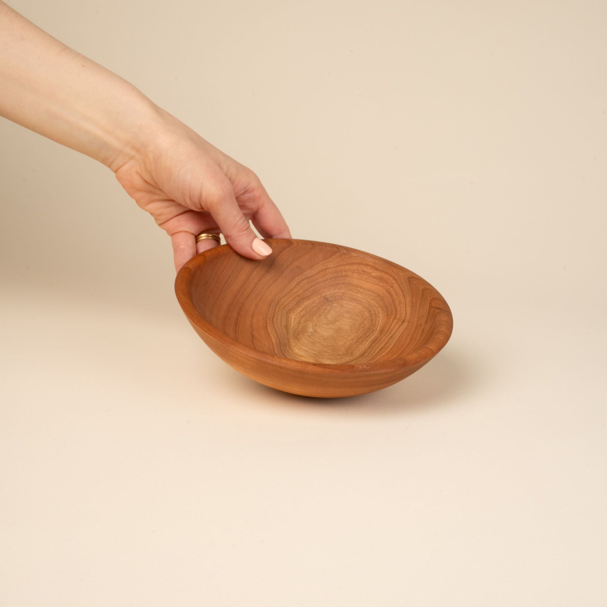 A hand holds out a small cherry wood bowl