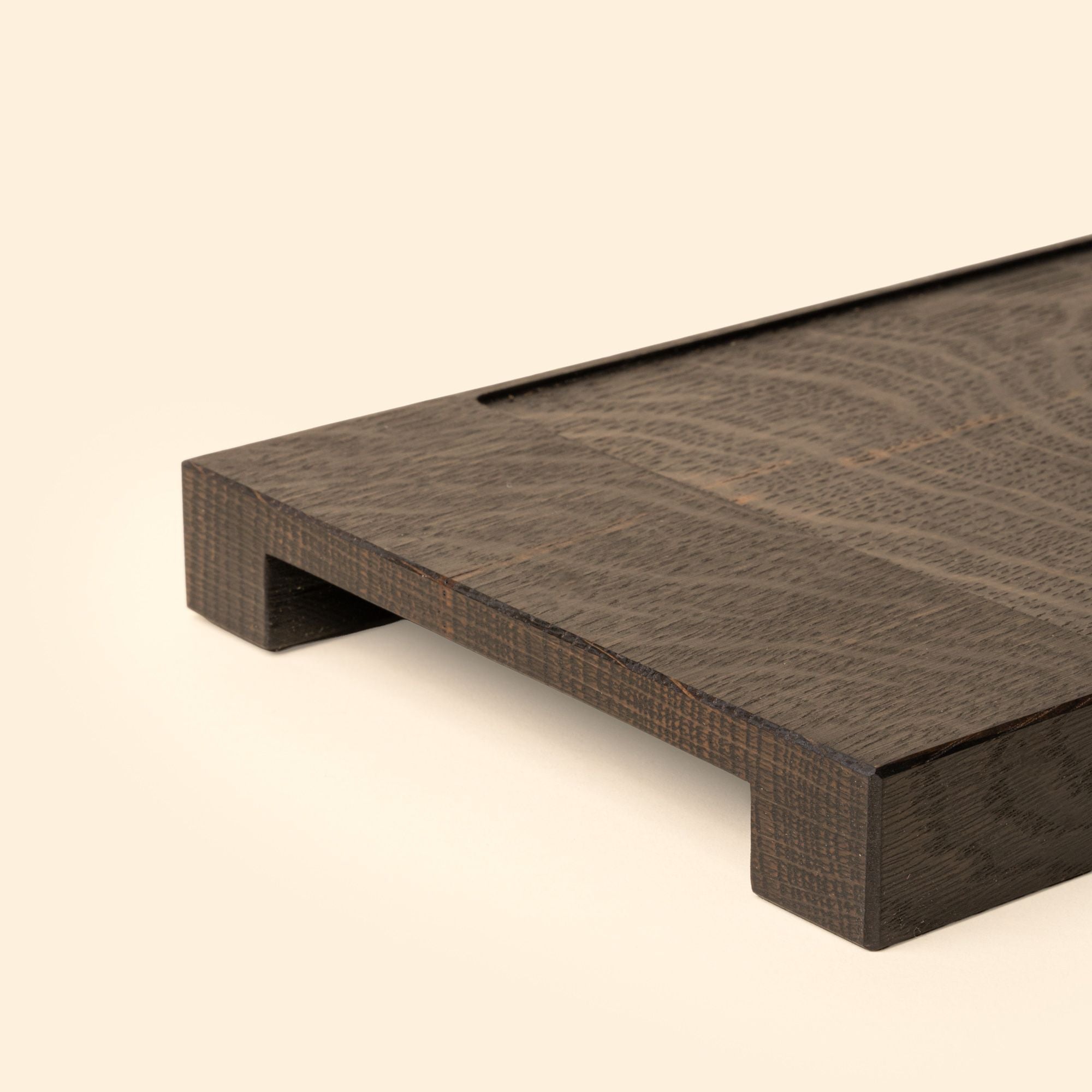 Close up of the handled edge of a narrow rectangle of ebonized oak wood with a vertical groove at either end