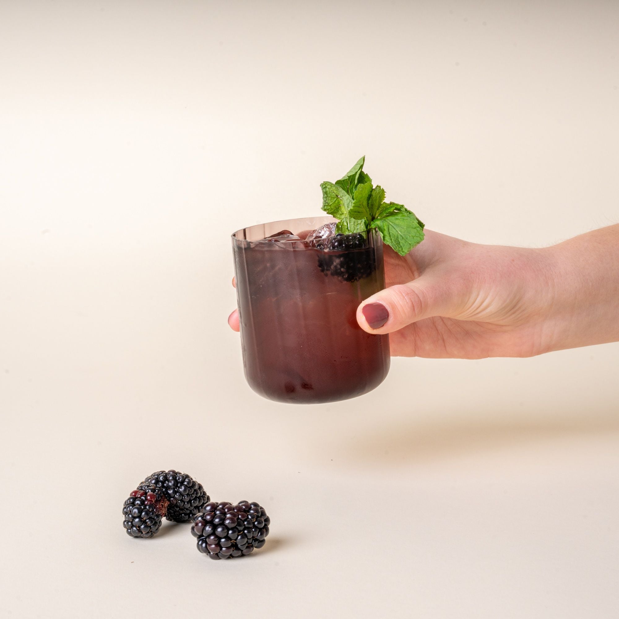 A hand holds a cocktail in a fluted walled tumbler in a grey purple color