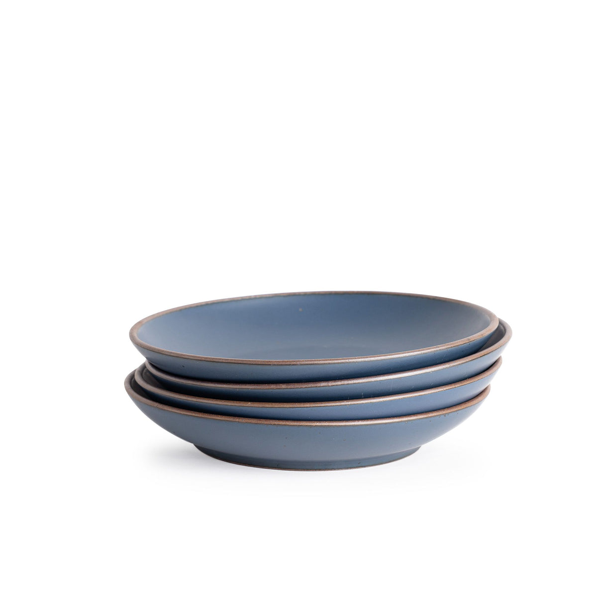 A stack of 4 large ceramic plates with a curved bowl edge in a cool, medium blue color featuring iron speckles and an unglazed rim.