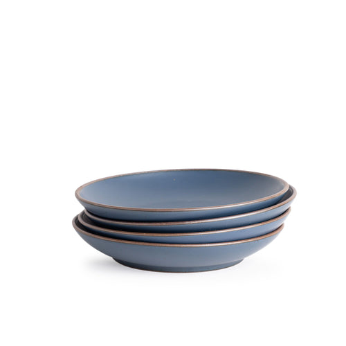 A stack of 4 large ceramic plates with a curved bowl edge in a cool, medium blue color featuring iron speckles and an unglazed rim.