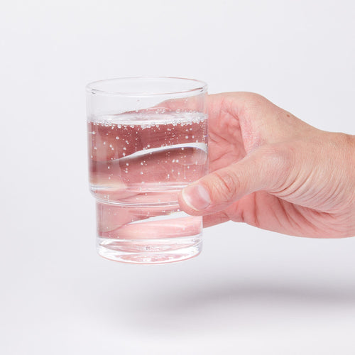 Hand holding a clear cylindrical glass with a wider top half with a narrower bottom half, full of water