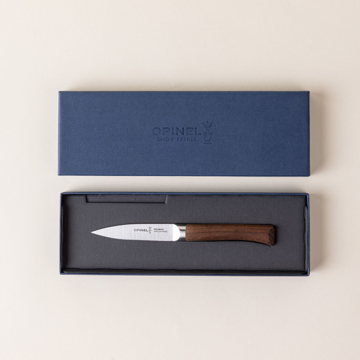 A small paring knife with a sharp steel blade and a beveled dark wood handle sitting in a packaged box