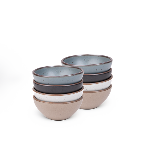 A stack of 8 small dessert sized rounded ceramic bowls in a blue-grey, graphite black, cool white, and warm pale brown colors featuring iron speckles and an unglazed rim