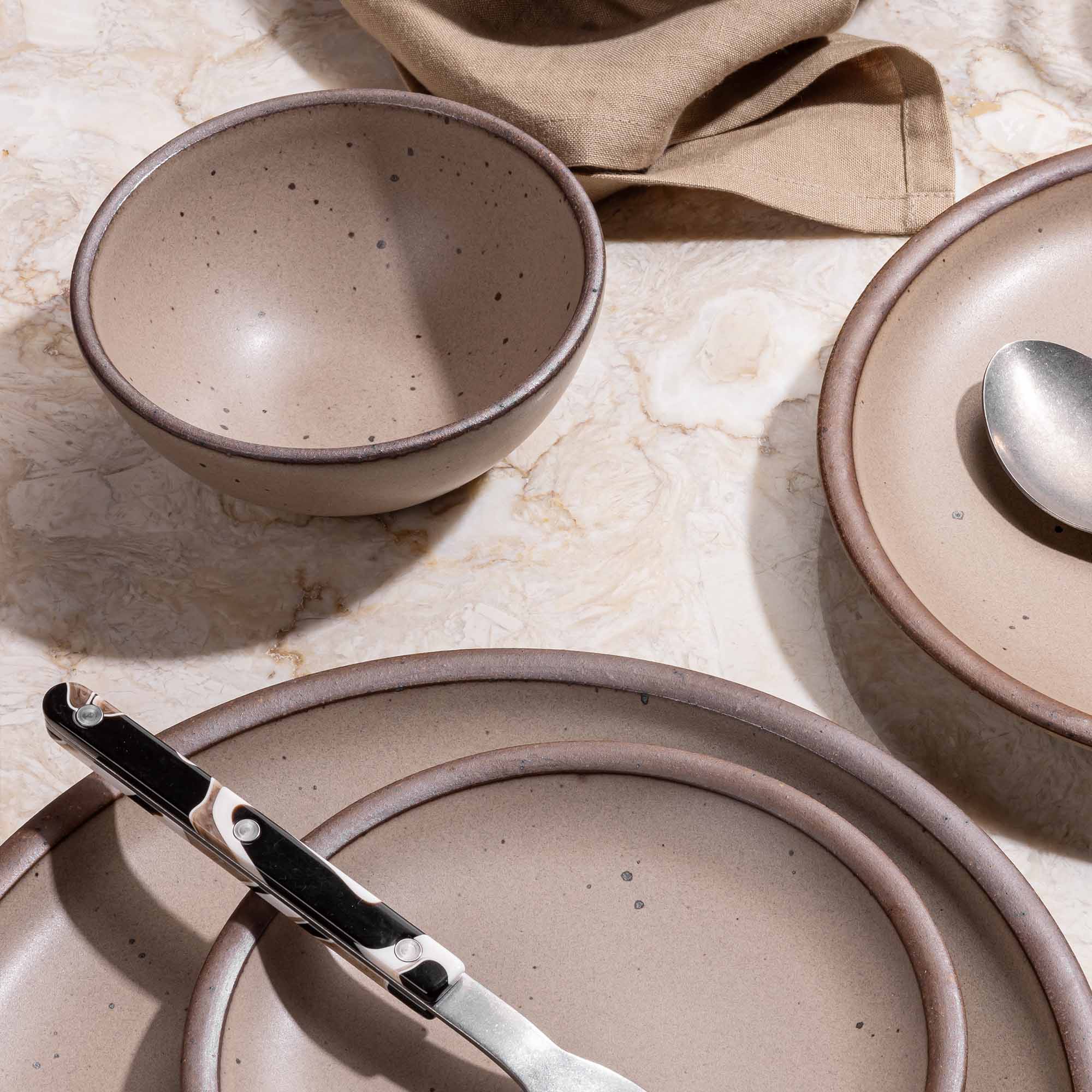 A small rounded dessert bowl in a muted brown with ceramic plates in the same color