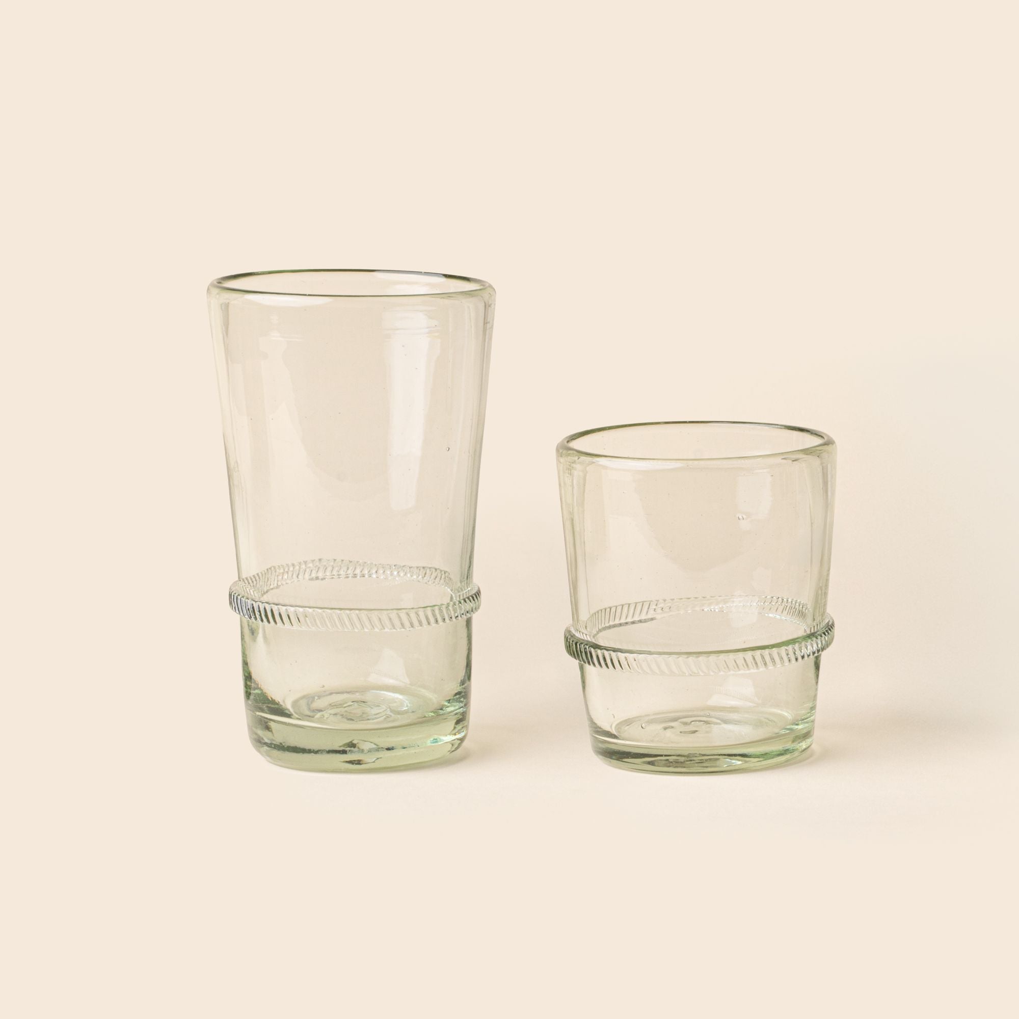A clear short and tall recycled glass tumblers with a ridged band detail.