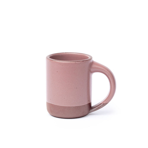 A medium sized ceramic mug with handle in a dusty mauve pink color featuring iron speckles and unglazed rim and bottom base.