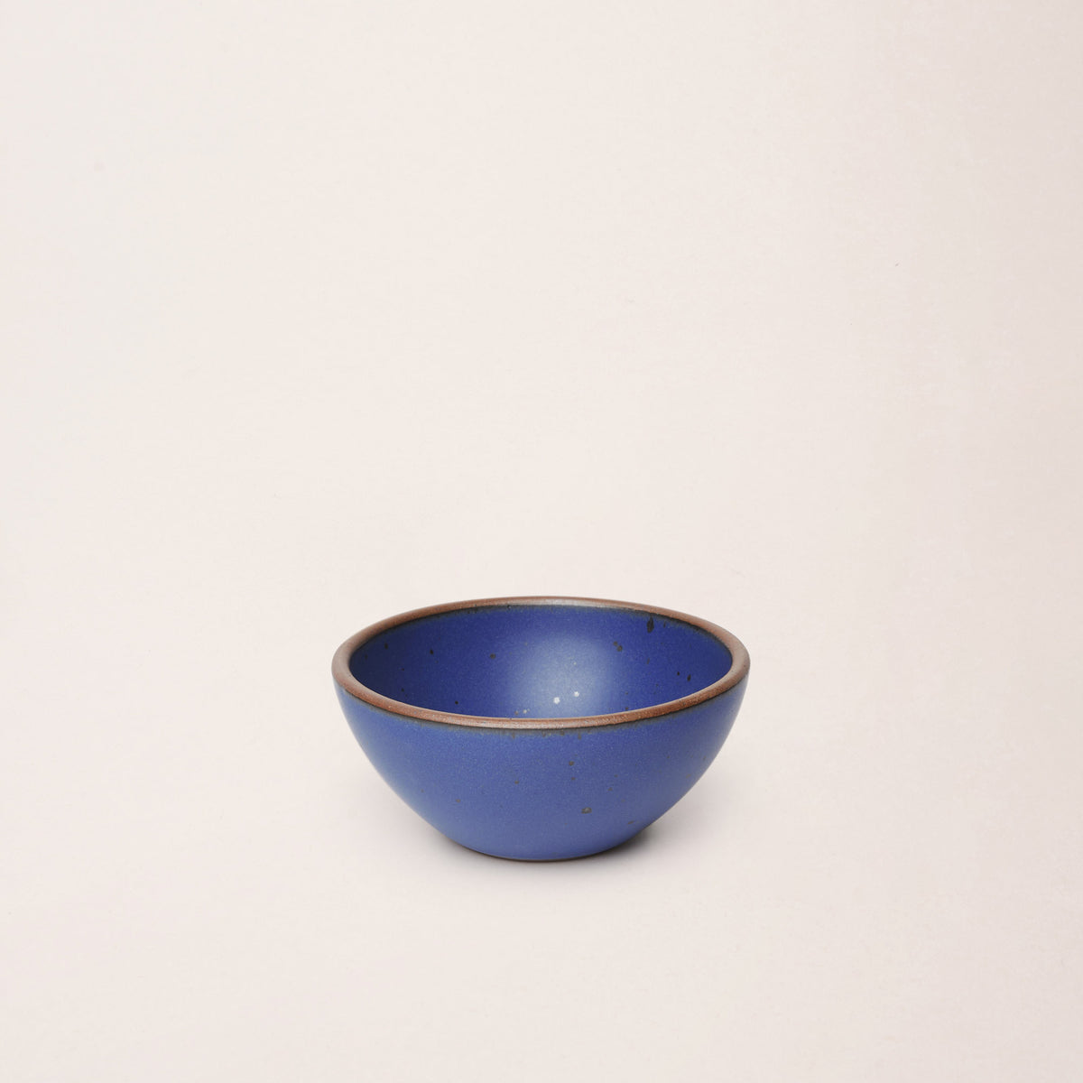 A small dessert sized rounded ceramic bows in a cobalt blue color featuring iron speckles and an unglazed rim