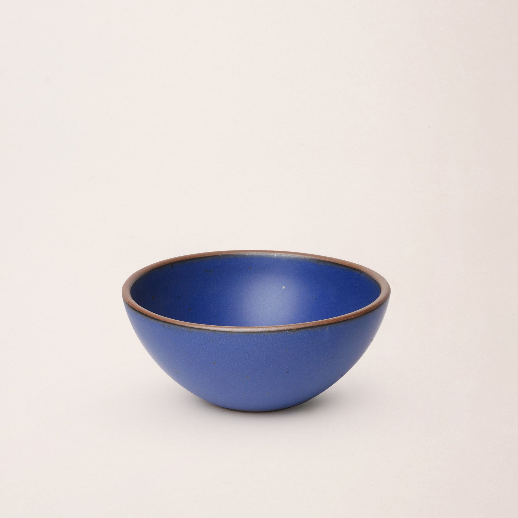 A medium rounded ceramic bowls in a cobalt blue color featuring iron speckles and an unglazed rim